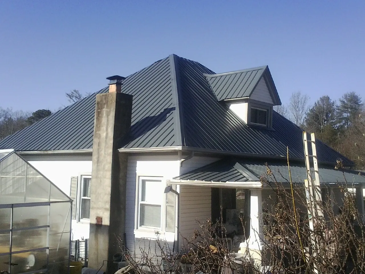 Dark blue standing seam metal roof on a white farmhouse with dormer in Berlin